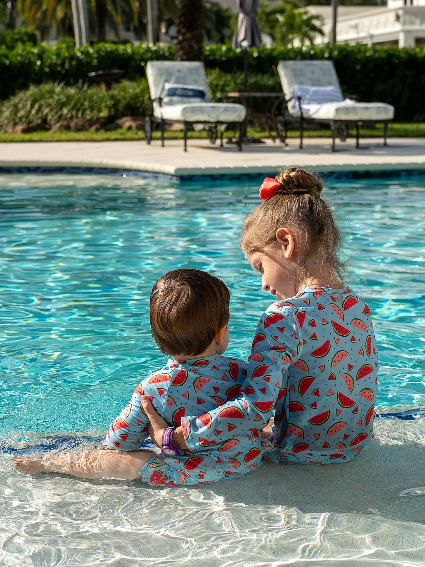 Girl in Isla & Ray watermelon print rash guard swimsuit matching with baby boy in watermelon rash guard sunsuit