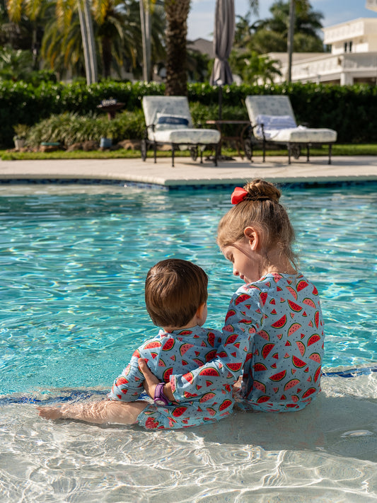 Girl in Isla & Ray watermelon print rash guard swimsuit matching with baby boy in watermelon rash guard sunsuit