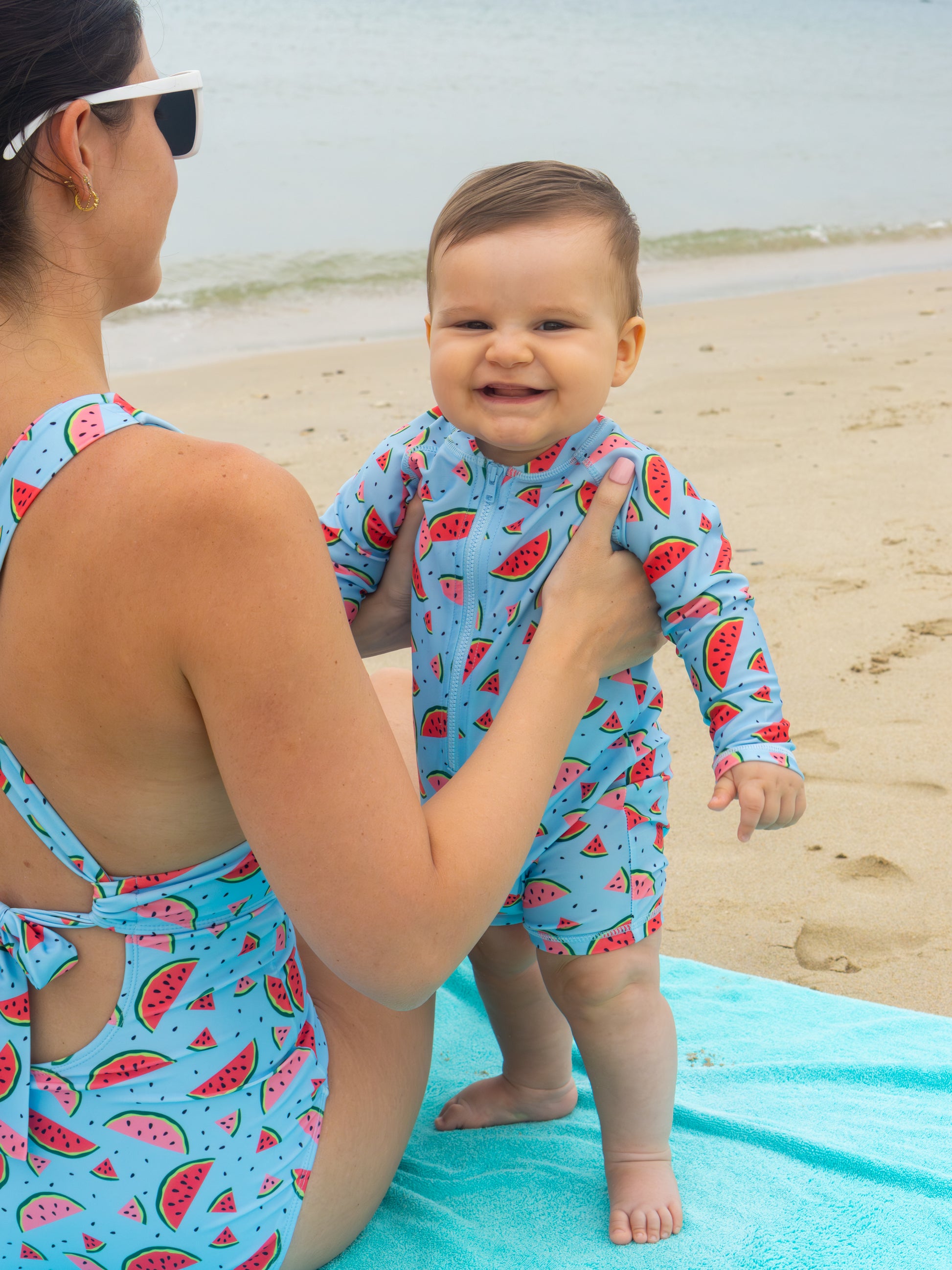 Baby boy wearing watermelon print rash guard sunsuit by Isla & Ray at beach with Mom